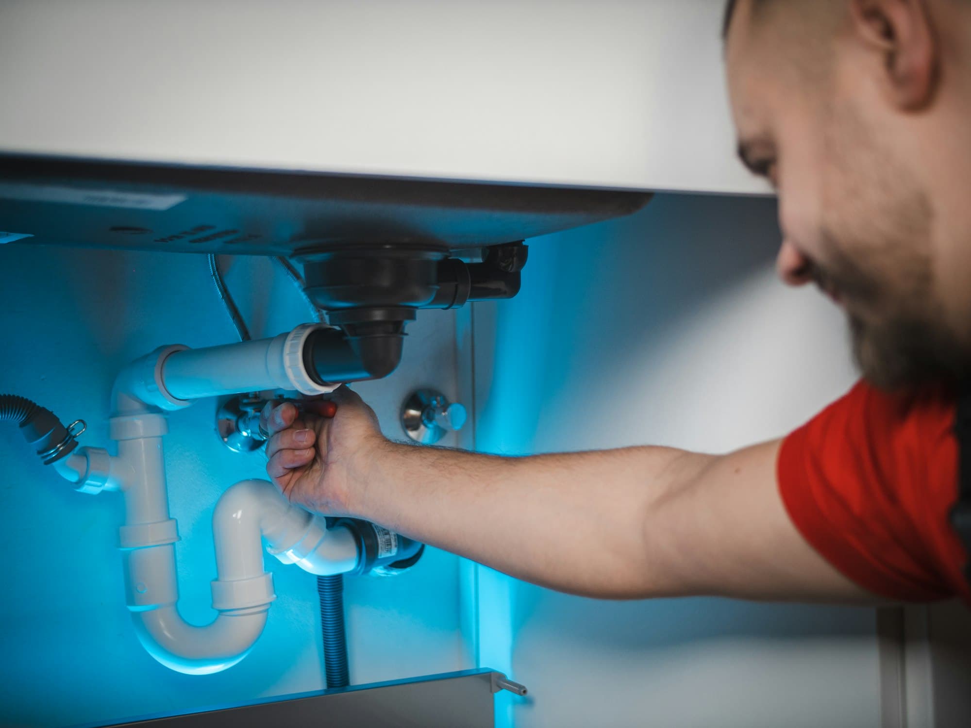 Plumber working on drain pipes under a sink